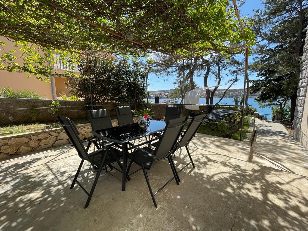Terrace of the BeachHouse with a dining table and six chairs under a vine pergola, the bay of Šilo behind
