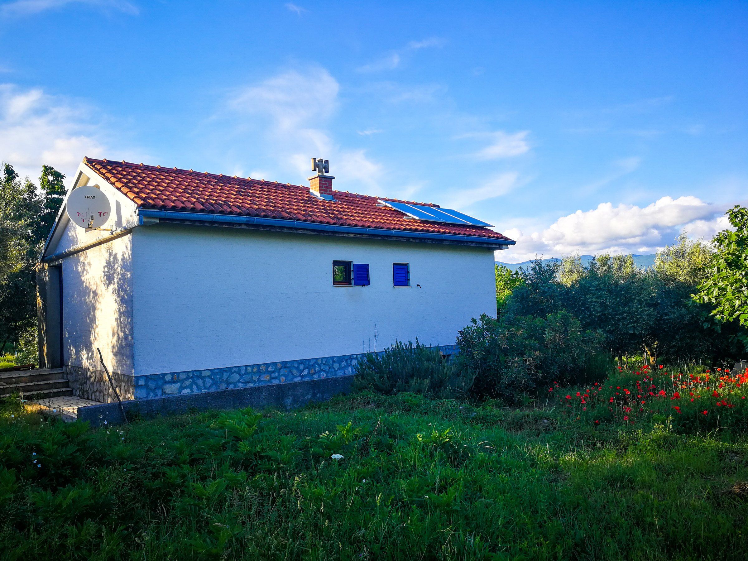 The EcoHouse, a white single-storey house with a red tiled roof and solar panels, in a green garden